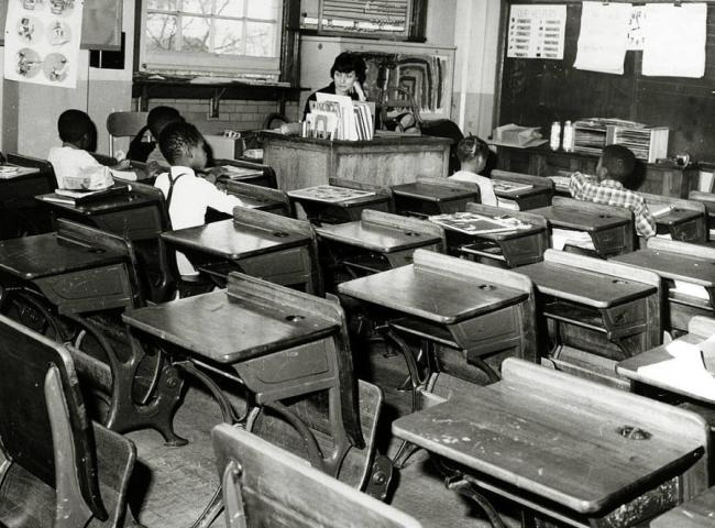 Photo of a large classroom containing only a few Black students and one white teacher